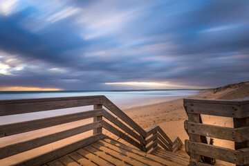 Wooden viewpoint at a beach surrounded by the sea under a cloudy sky with long exposure - obrazy, fototapety, plakaty