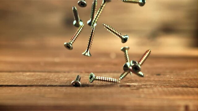 Self-tapping screws fall on the table. On a wooden background. Filmed is slow motion 1000 frames per second.