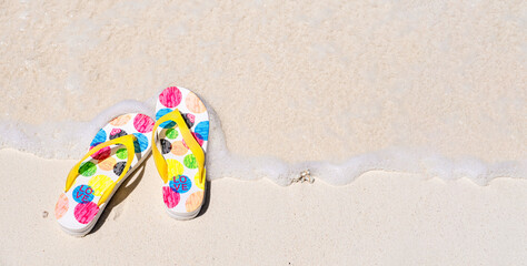 Summer flop flops or sandals on sandy beach by sea water, top view, copy space