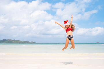 A happy young girl of thirteen, wearing a red Father Christmas hat, jumps for joy and fun on a tropical beach, the concept of summer holidays. Copy space