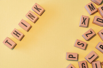 Word THINK taken from a pile of wooden letter blocks with yellow background and copy space