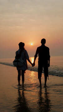 Young happy couple standing on seashore during sunrise time at Kuakata sea beach, Bangladesh. A newly married couple is watching sun rising holding their hands