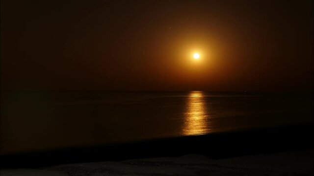 time-lapse. moon path. night. the moon rises over the sea.