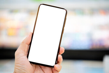 Hand holding smartphone with blurred supermarket aisles background. Online shopping concept.