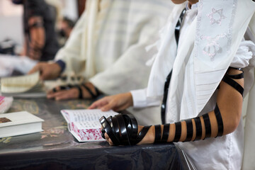 Close up, young men reading Jewish prayer and a hand with tefillin and talit.Selective focus. Soft focus