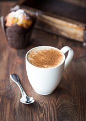 cup of cappuccino with cinnamon and blueberry muffin in the background