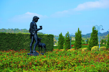 Fototapeta na wymiar A sculpture of a roman angel standing with a little deer in garden under blue sky background