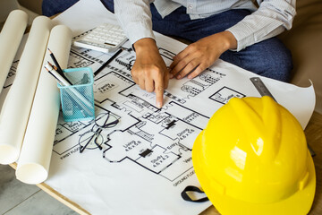 Young engineer pointing finger at a building on blueprints for a workplace meeting, engineer's hand working with tools on a background on a project draft.