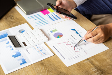 Young businessman pointing to last quarter's earnings and comparing data in smartphone in hand, businessman pointing to past company volatility, business idea planning.