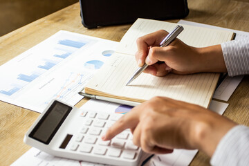 Young businessman calculates company income data and writes it down in a notebook to bring to meetings, businessman pointing to past company figures, business idea planning.