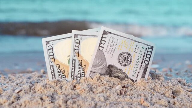 Three one hundred dollar bills half buried in sand on sandy seashore close-up. Three paper dollar bills half in sand on sea beach. Concept money, finance, investment, wealth, poverty, financing, cash