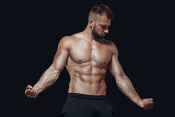 Young muscular and fit young bodybuilder fitness male model posing and demonstrating his muscles isolated on black background