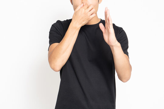 白い背景の前に立って、悪臭に困って鼻をつまむポーズをする黒いTシャツを着ている男性
