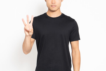 白い背景の前に立って、手で数字の3を表す黒いTシャツを着ている男性