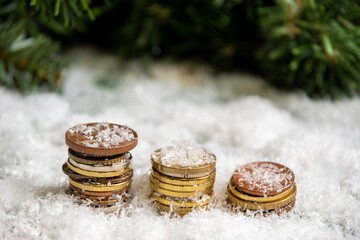 A golden pyramid of coins covered with snow against a background of green spruce branches. Success concept. Savings concept. Wealth concept in the new year