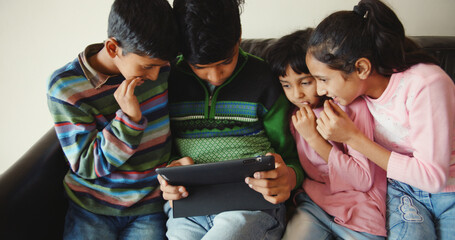 Closeup of four South Asian siblings watching videos on a tablet at home