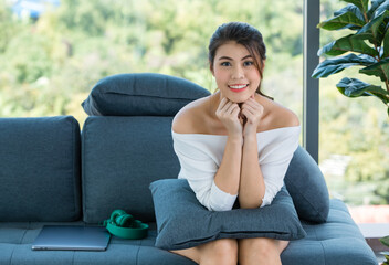 Obraz premium Portrait shot of Asian beautiful happy cheerful teenager female housewife in casual outfit sitting on cozy sofa couch with pillows holding fists at chin take break from studying online on laptop