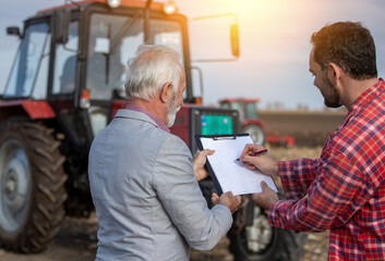 Male farmer signing a contract with insurance agent at agricultural field. - obrazy, fototapety, plakaty