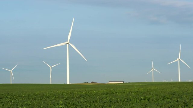 Wind turbines in a green field; turning blades of turbines with clear blue sky on early summer morning. 223