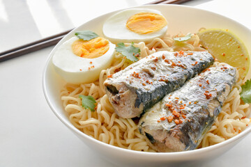 Instant noodles with sardines, boiled egg, lime, red chilli flakes and coriander in a white bowl.