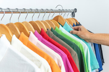 MALE HAND TAKING COLORED POLO SHIRTS ON HANGERS IN THE CLOSET, WARDROBE, DRESSING ROOM OR STORE. SALES, MENSWEAR AND SHOPPING CONCEPT.