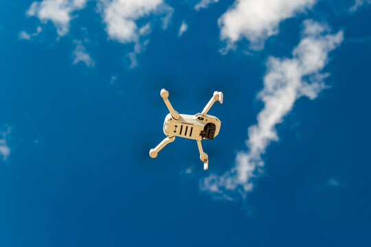 Small white drone DJI Mini 2 in flight against blue sky, bottom view: Russia - May 2021