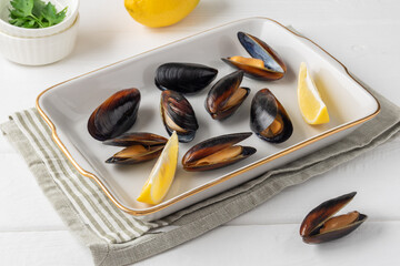 Mussels, lemon and two white bowls with parsley  are on white wooden table. Copy space.