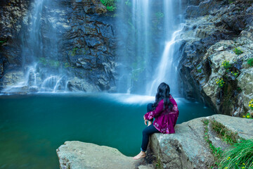 young girl watching waterfall falling from mountain with calm blurred water surface at morning