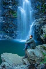 young man at waterfall falling from mountain with calm blurred water surface at morning