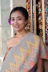 Portrait young woman with balinese face, wearing dress traditional Bali sarong in home door.