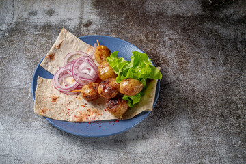 Serving a dish from a restaurant menu. Grilled country-style baked potatoes with pita bread, herbs and onions on a blue plate against the background of a gray stone table