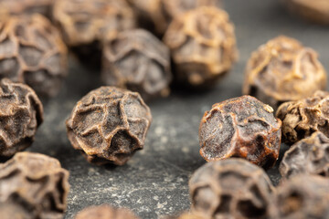 Close up view of true edible spices and seeds: Magnified black peppercorn (Piper nigrum)  on a black stone surface