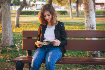Obraz premium Cheerful teenager girl reading book on the bench at autumn park