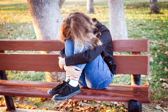Sad teenager girl sitting on the bench in autumn park. Crying young girl in depression