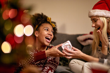 A girl is giving a present to her female friend at New Year party at home. Christmas, New Year, holiday, party - Powered by Adobe