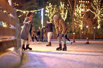 A young couple in love has a good time while skating at ice-skating rink during christmas holidays in the city. Christmas, New Year, holiday, love