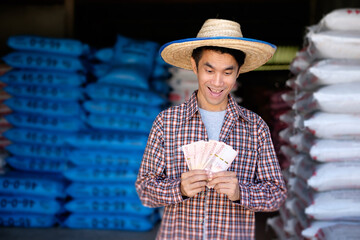 Asian farmer man holding Thailand banknote money with wow shock face at chemical fertilizer store...