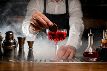 backlit glass with red alcoholic cocktail which the male bartender gently decorates