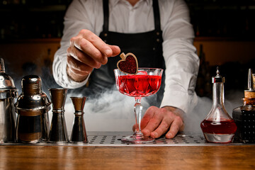 close-up of glass with alcoholic cocktail which the male bartender gently decorates with small wooden pin