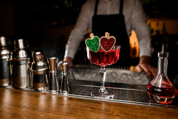 Close-up of glass with delicious tasty red alcohol cocktail decorated with small wooden green and red hearts.