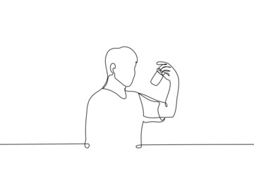 man stands looking at a jar of tablets or pills - one line drawing vector. concept of buying medicines, reading the composition of ingredients from medicines and supplements