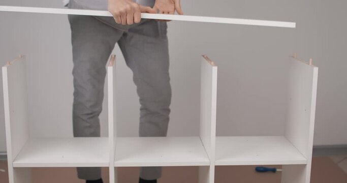 The guy inserts an unworthy wooden shelf in the process of assembling a wooden shelf. Indoors. Prores.