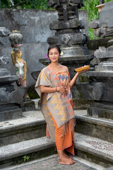 Portrait young woman with balinese face, wearing dress traditional Bali sarong in home temple. 