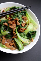 Kimchi cabbage in a bowl with beef over top with chopsticks on dark background, Korean food, top view
