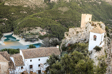 Fototapeta na wymiar Guadalest village surrounded by vegetation, the reservoir and the Castle and bell tower