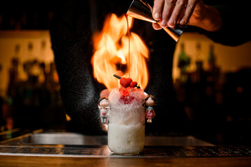 bartender holds jigger in his hand and skillfully fills cocktail glass with syrup