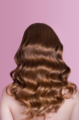 Hollywood wave styling on long beautiful red hair, back side view of red-haired young lady with long hair isolated on pink background