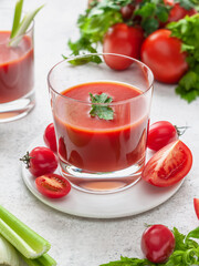 Tomato juice in a glass surrounded by tomatoes and fresh herbs on a light background, vertical