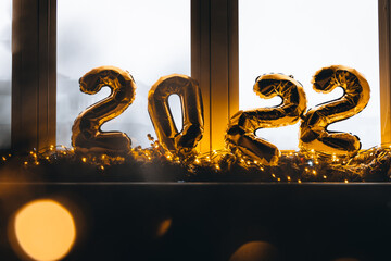 2022 golden foil balloons on blue window sill. Celebrating holidays at home, festive decor concept....