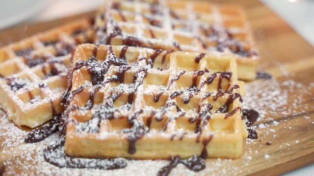 Closeup of adding icing sugar on chocolate waffles in a bakery cafeteria.